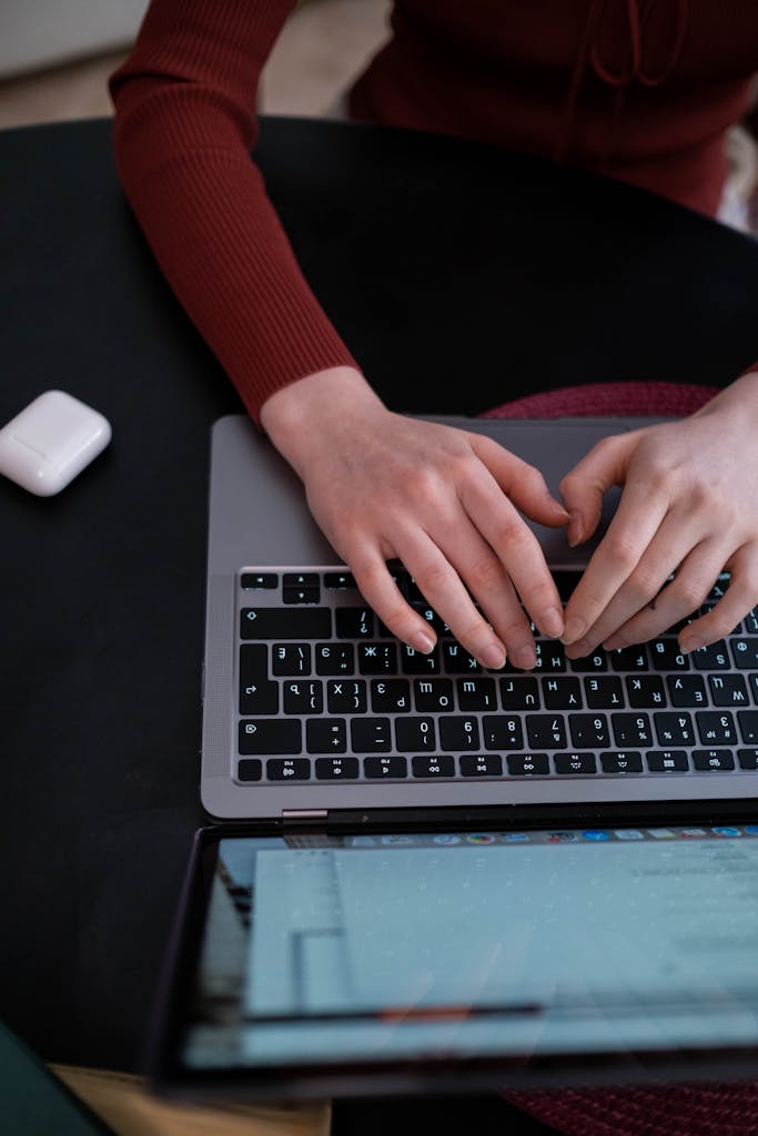 Person typing on a laptop keyboard indoors with AirPods nearby